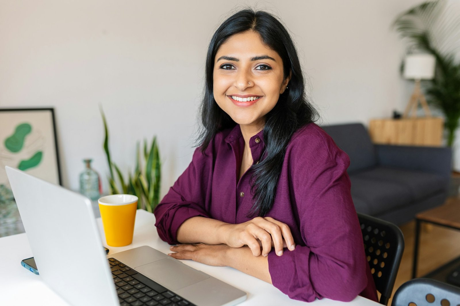 Young indian woman smile at camera working with laptop at home